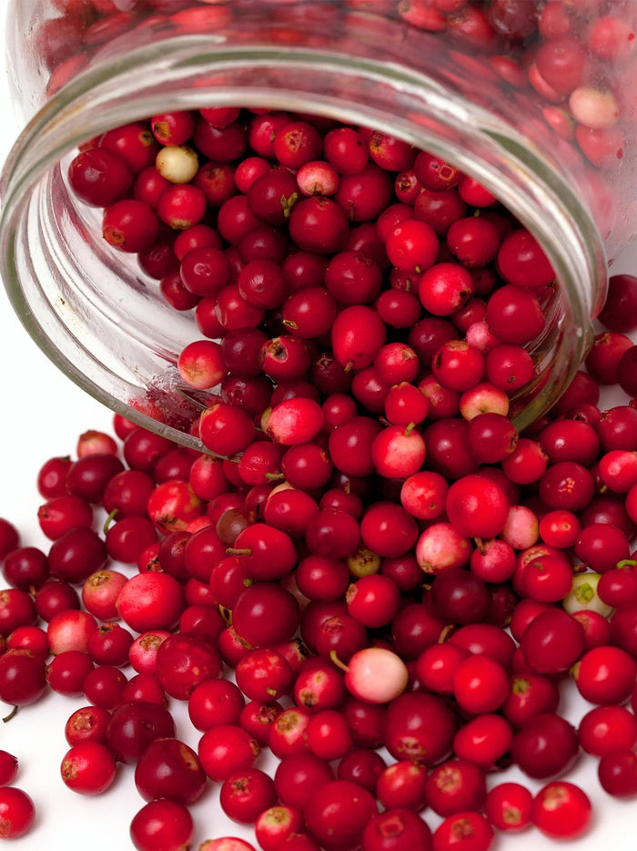 Glass jar filled with red berries spilling out on a white background