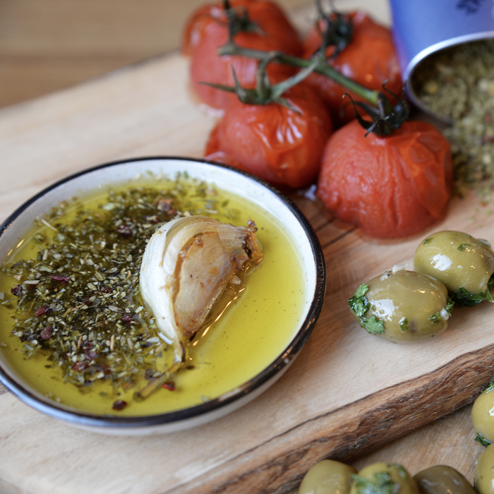 Wooden board with olives, tomatoes, and a dish with olive oil, herbs, and a garlic clove.