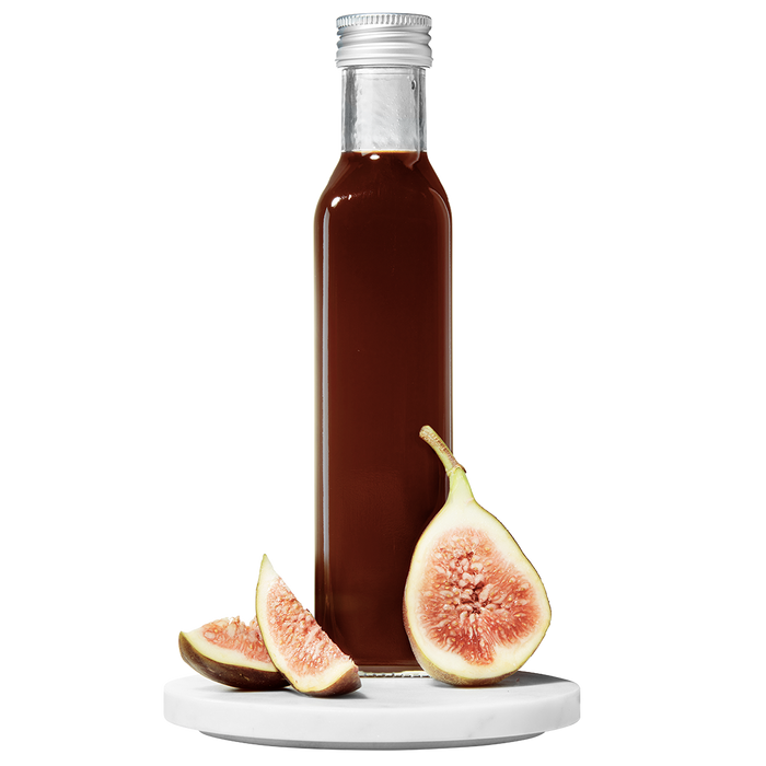 A bottle of Fig Balsamic Vinegar with a fig and slices of fresh fig placed in front of the bottle.