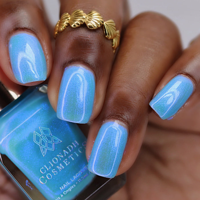 Close-up of nails painted with Ginto Nail Lacquer on deep skin tone. Hand is holding polish bottle.