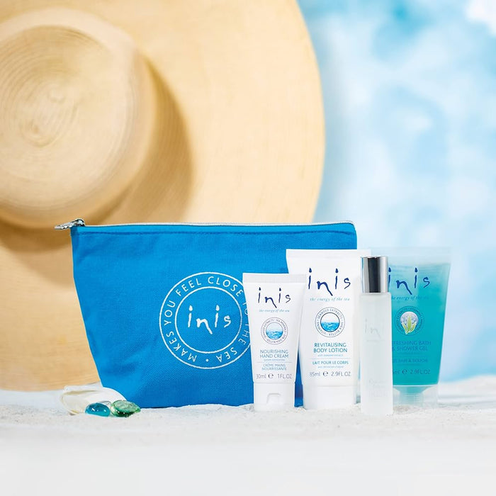 Inis skincare products with a blue pouch on sand and straw hat in the background