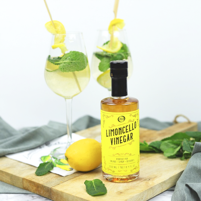 Limoncello Vinegar on a wooden board with two limoncello vinegar spritzes garnished with mint in the background