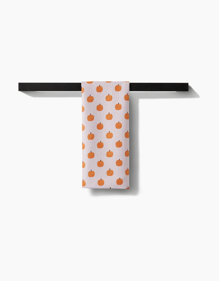 Towel with orange pumpkin pattern hanging on a black rack against a white background