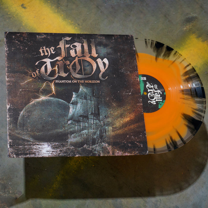 A limited edition vinyl by The Fall of Troy, Phantom on the Horizon, with a black splatter and clear & orange mix, is partially out of its sleeve. The album art shows a ghostly ship on a dark, cloudy sea.