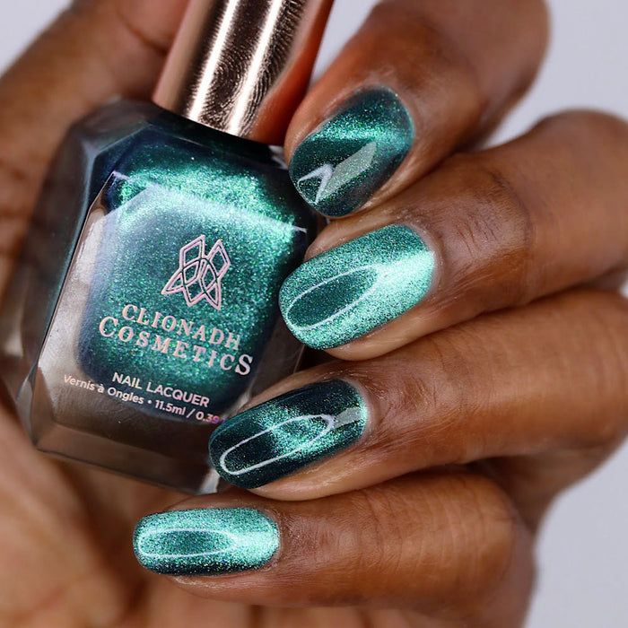 Close-up of nails painted with Turquoise Silk Nail Lacquer on deep skin tone. Hand is holding polish bottle.
