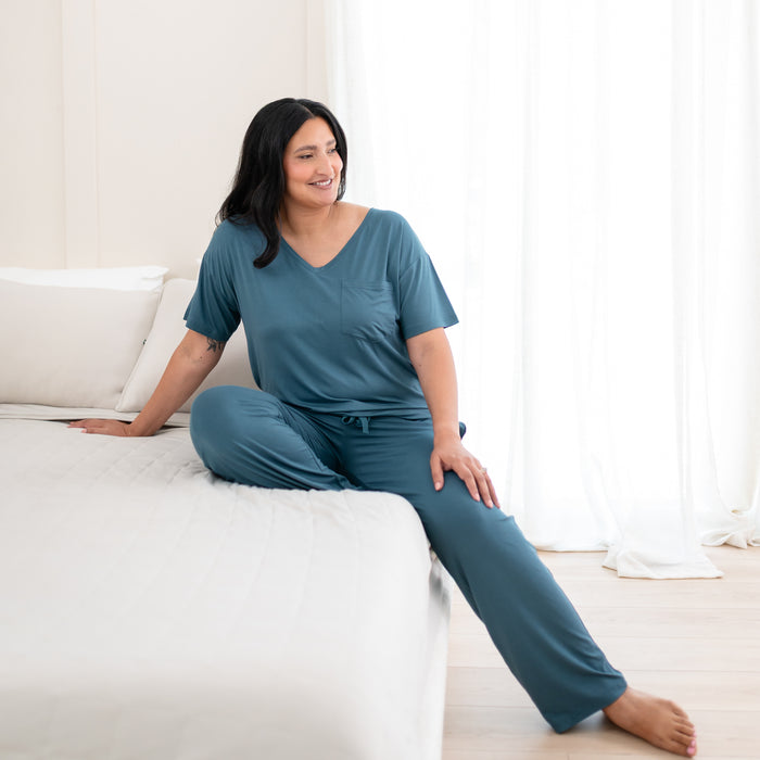 Female model sitting on a bed wearing the Women’s Relaxed Fit V-Neck in Atlantic with matching women's lounge pants