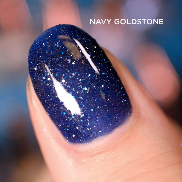 Close-up of one nail painted with navy Goldstone Nail Lacquer, on a dark blurred background.