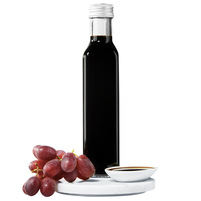 A dark bottle of balsamic vinegar with a silver cap, accompanied by a small bunch of red grapes.