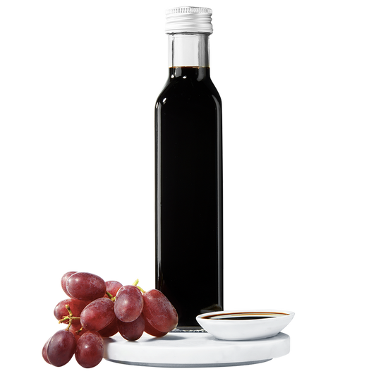 A dark bottle of balsamic vinegar with a silver cap, accompanied by a small bunch of red grapes.