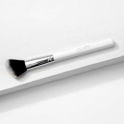 ColourPop Angled Face Brush makeup brush resting diagonally on a white textured platform, featuring a white handle with ColourPop logo, shiny silver ferrule, and soft black-to-white angled bristles for precise blush, bronzer, and contour.