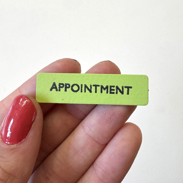A small rectangular lime green magnet with the word 'APPOINTMENT' in black capital letters, held between fingers against a plain white background.