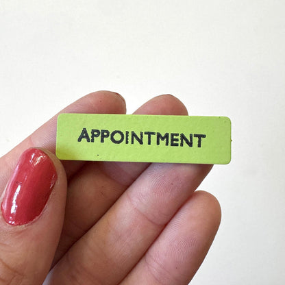 A small rectangular lime green magnet with the word 'APPOINTMENT' in black capital letters, held between fingers against a plain white background.