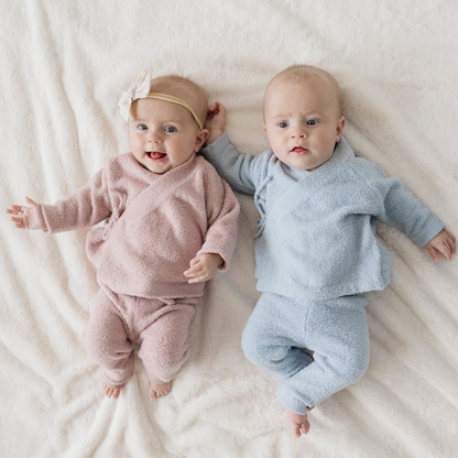 Two babies in pink and blue outfits lying on a white blanket