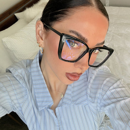 lifestyle - emily gordon brunette influencer wearing light blue cotton blouse with oversized black cat eye eyeglasses