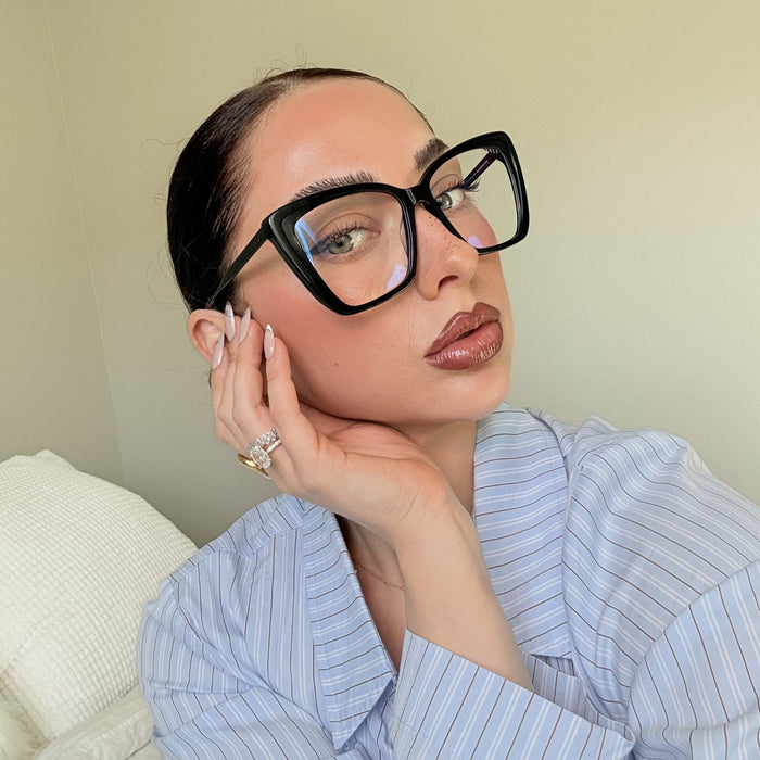 lifestyle - emily gordon brunette influencer wearing light blue cotton blouse with oversized black cat eye eyeglasses