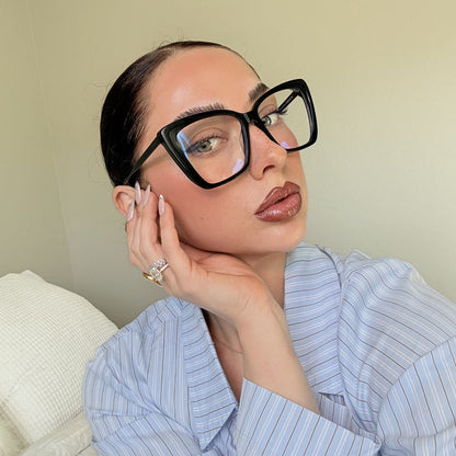 lifestyle - emily gordon brunette influencer wearing light blue cotton blouse with oversized black cat eye eyeglasses