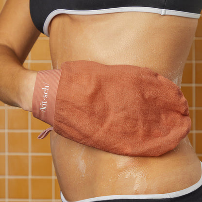 Close-up of model using the Kitsch Terracotta Exfoliating Glove to scrub their torso in the shower against a yellow tile background