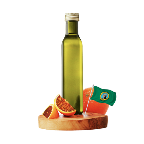 A tall green glass bottle of olive oil with a silver cap, standing on a round wooden board with sliced oranges and a small flag, against a plain white background.