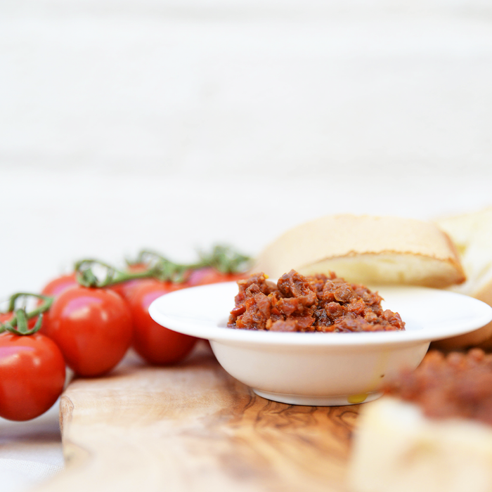 small white bowl of bruschetta on a wooden surface with tomatoes in the background