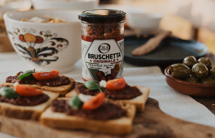 Jar of Bruschetta dried herbs on a table with bruschetta on toasts in the foreground and olives in the background in a small dish