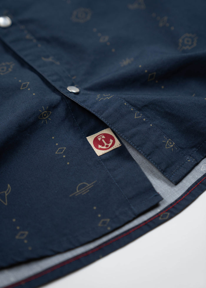 Navy blue shirt with subtle geometric patterns, silver buttons, and a red logo tag peeking from the hem.