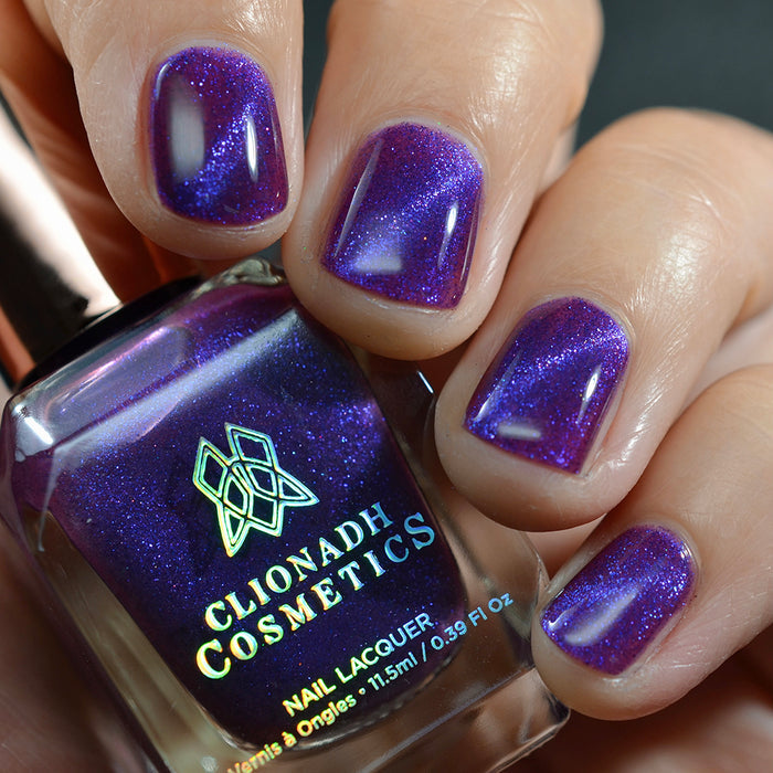 Close-up of nails painted with Butterfly Pea Flower Nail Lacquer on fair skin tone. Hand is holding polish bottle.