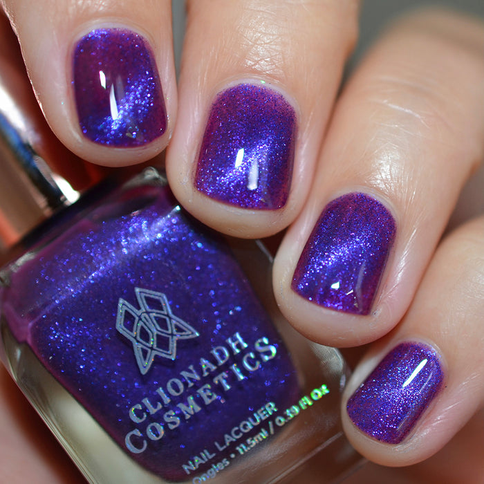 Close-up of nails painted with Butterfly Pea Flower Nail Lacquer on fair skin tone. Hand is holding polish bottle.