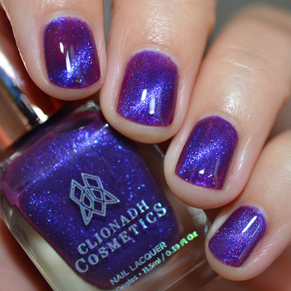 Close-up of nails painted with Butterfly Pea Flower Nail Lacquer on fair skin tone. Hand is holding polish bottle.