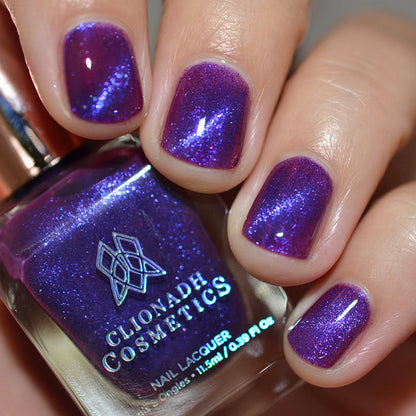 Close-up of nails painted with Butterfly Pea Flower Nail Lacquer on fair skin tone. Hand is holding polish bottle.