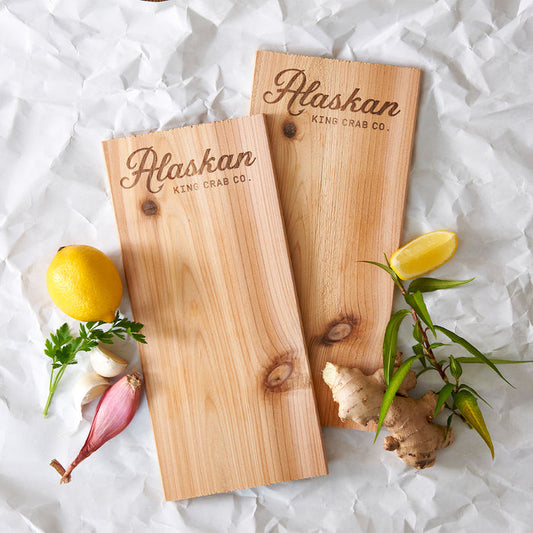 Two wooden cutting boards with 'Alaskan King Crab Co.' branding on a white background with vegetables.
