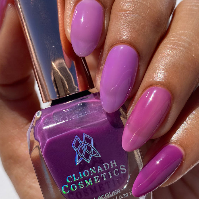 Close-up of nails painted with Cirrus and Euphoric Nail Lacquer on medium skin tone. Hand is holding polish bottle.