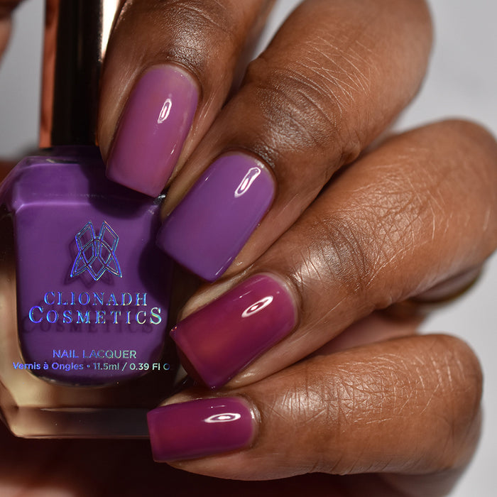 Close-up of nails painted with Cirrus and Euphoric Nail Lacquer on deep skin tone. Hand is holding polish bottle.