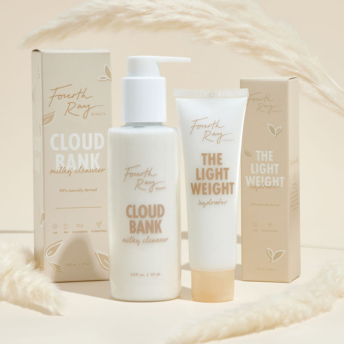 Cloud Bank Milky Cleanser pump bottle by Fourth Ray Beauty stands beside its box, flanked by The Light Weight Hydrator on a beige set with pampas, showcasing a 5.8 fl oz ColourPop Face Cleanser with a 98% naturally derived formula.