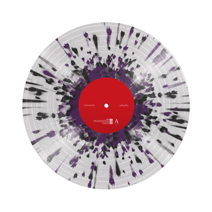 Clear vinyl record against a white background, with black and purple splatters, with a red label in the center.