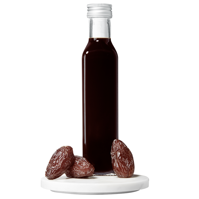 A bottle of Date Balsamic Vinegar with several dates placed in front of the bottle on a white surface.