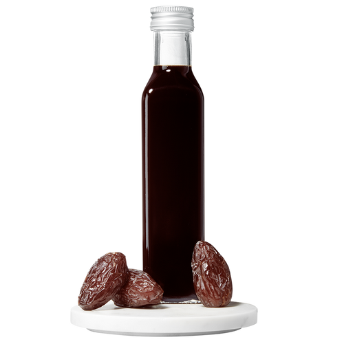 A bottle of Date Balsamic Vinegar with several dates placed in front of the bottle on a white surface.