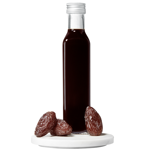 A bottle of Date Balsamic Vinegar with several dates placed in front of the bottle on a white surface.