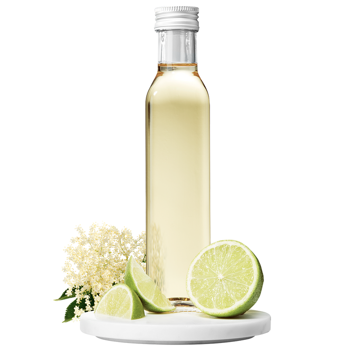 A bottle of Elderflower Apple Lime Vinegar with a cap, accompanied by elderflower blossoms and lime slices.