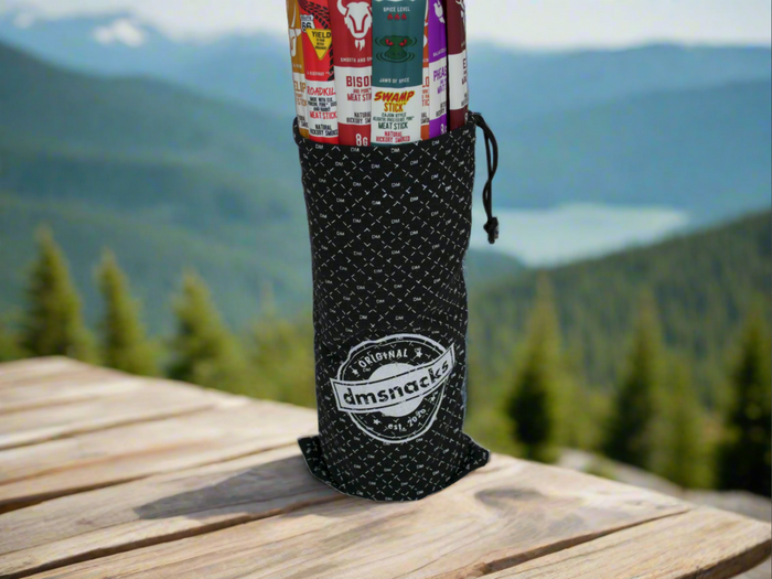 Exotic Meat Sticks Bag with 14 Wild Beef Jerky Snacks in Stylish Canvas Bag on Outdoor Table with Scenic Mountain View