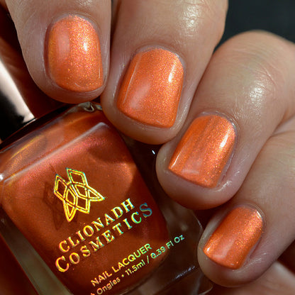 Close-up of nails painted with Fall Festival Nail Lacquer on fair skin tone. Hand is holding polish bottle.