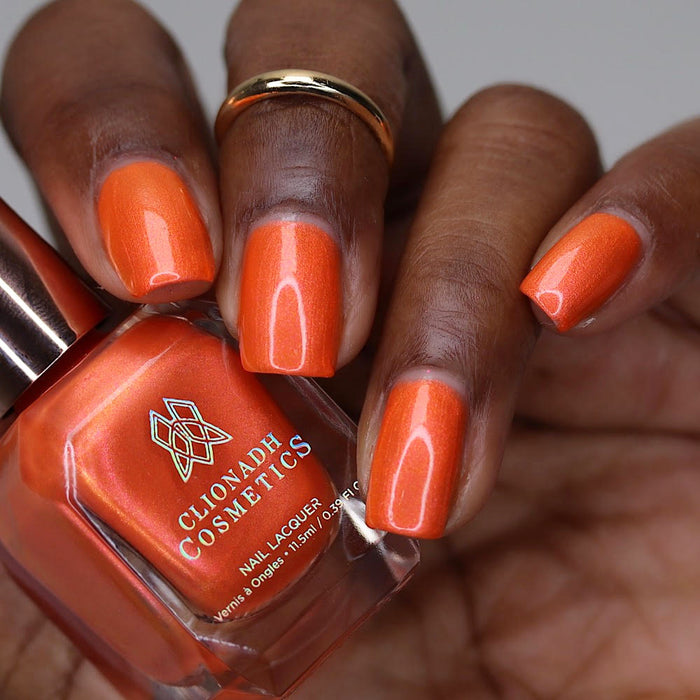 Close-up of nails painted with Fall Festival Nail Lacquer on deep skin tone. Hand is holding polish bottle.