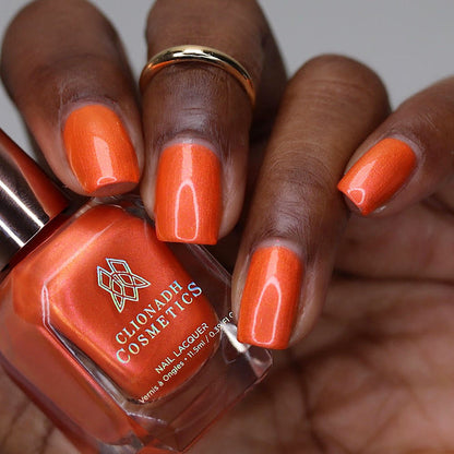 Close-up of nails painted with Fall Festival Nail Lacquer on deep skin tone. Hand is holding polish bottle.