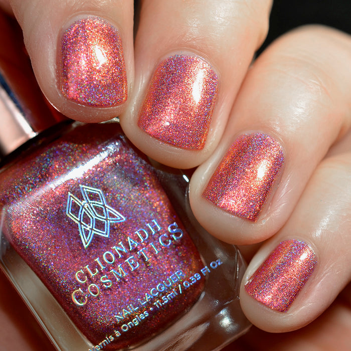 Close-up of nails painted with Flamin' Hot Holo Nail Lacquer on fair skin tone. Hand is holding polish bottle.