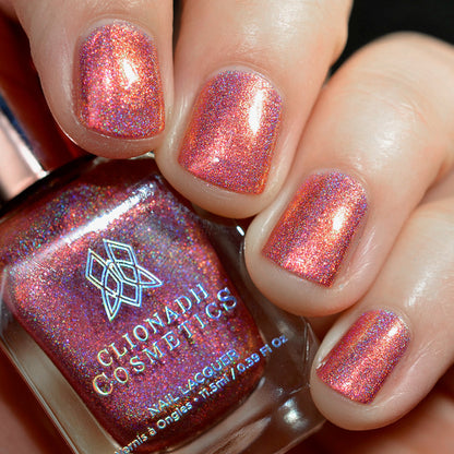 Close-up of nails painted with Flamin' Hot Holo Nail Lacquer on fair skin tone. Hand is holding polish bottle.