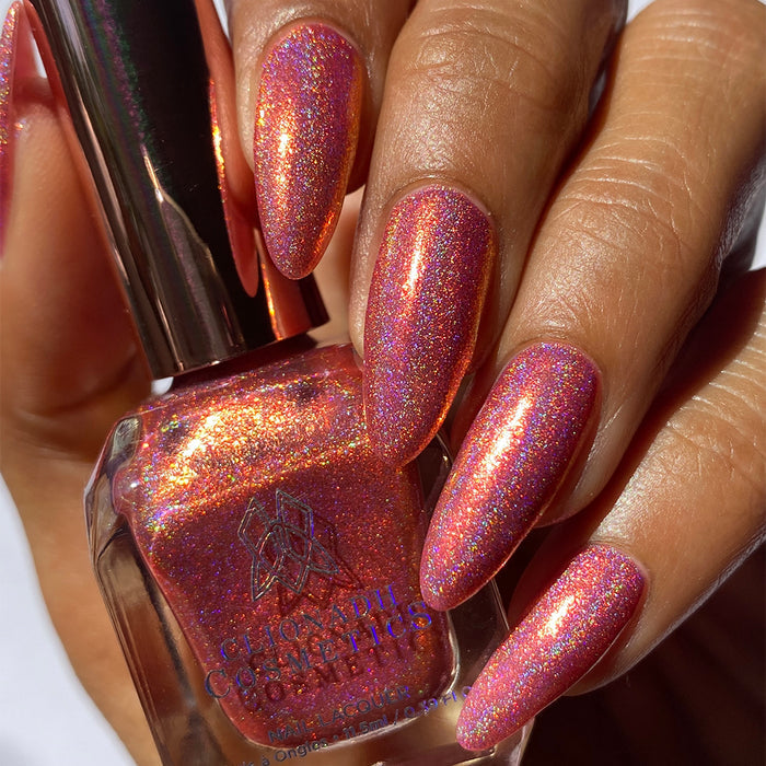 Close-up of nails painted with Flamin' Hot Holo Nail Lacquer on medium skin tone. Hand is holding polish bottle.