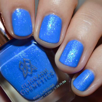 Close-up of nails painted with Frigid Nail Lacquer on fair skin tone. Hand is holding polish bottle.