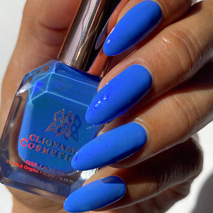 Close-up of nails painted with Frigid Nail Lacquer on medium skin tone. Hand is holding polish bottle.