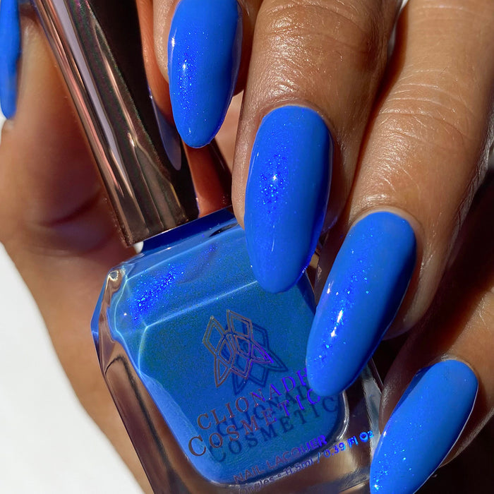 Close-up of nails painted with Frigid Nail Lacquer on medium skin tone. Hand is holding polish bottle.