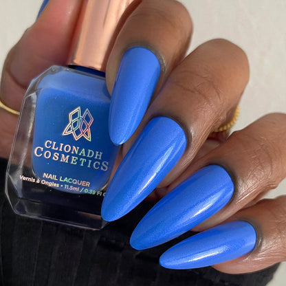 Close-up of nails painted with Frigid Nail Lacquer on deep skin tone. Hand is holding polish bottle.
