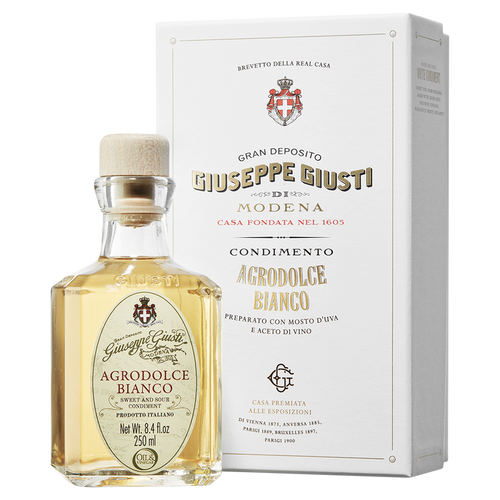 A bottle of Giuseppe Giusti Agrodolce Bianco di Modena balsamic vinegar next to its white gift box, both featuring the Giusti family crest.